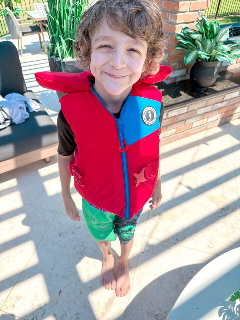 Wilder grinning in a red life jacket on a sunny pool deck